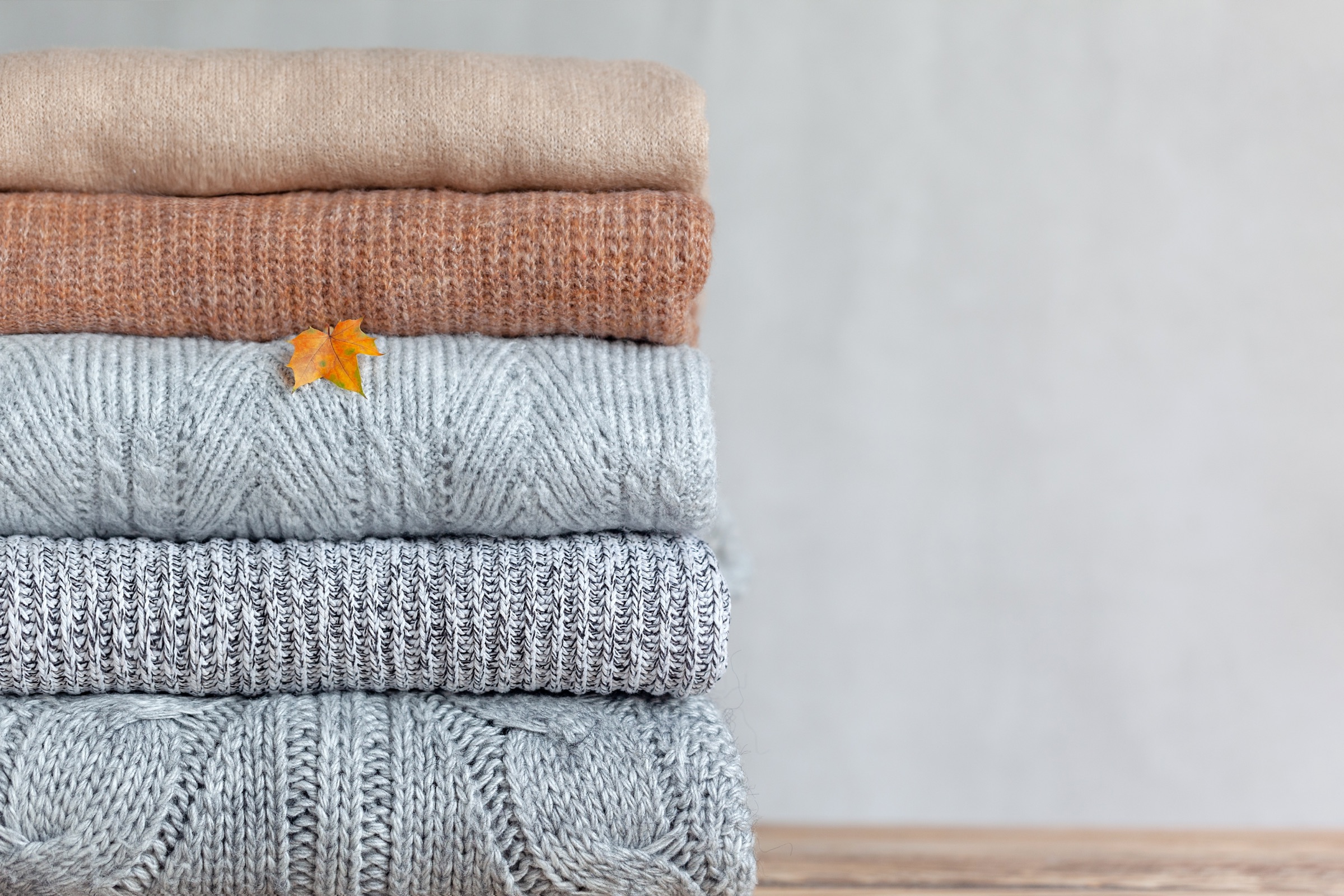 Stapel gefalteter Kaschmirpullover in Grau, Beige und Weiß auf hellem Untergrund